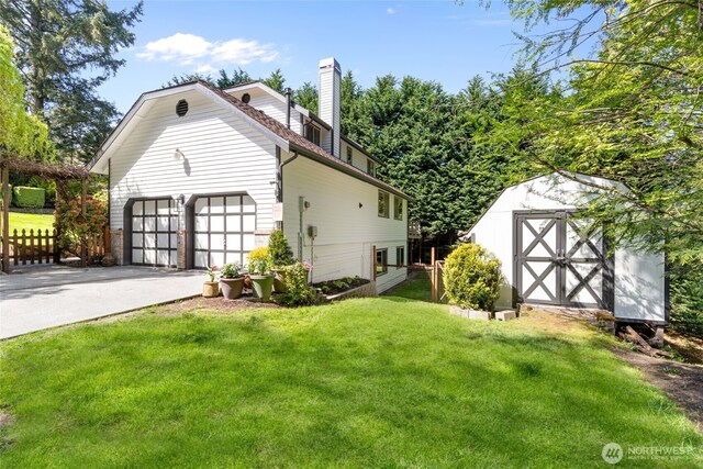 view of side of property featuring driveway, a chimney, a lawn, fence, and a storage unit