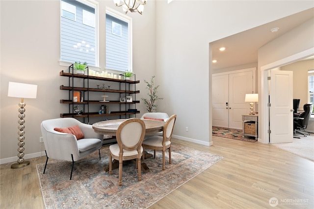 dining room with baseboards, a notable chandelier, a high ceiling, recessed lighting, and light wood-style flooring