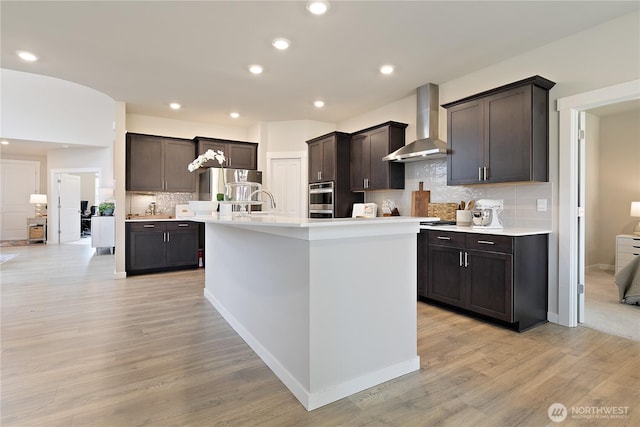 kitchen with light countertops, dark brown cabinets, wall chimney range hood, and tasteful backsplash