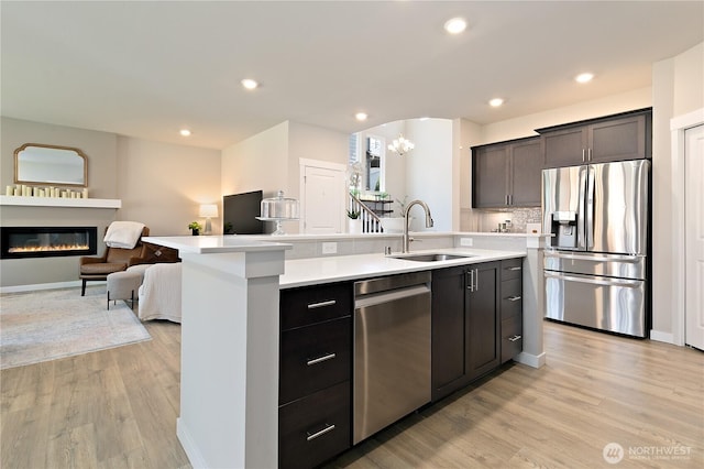 kitchen featuring appliances with stainless steel finishes, a sink, light countertops, open floor plan, and an island with sink