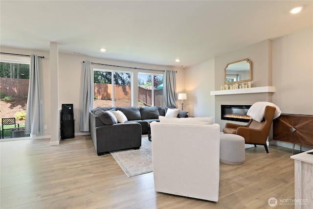 living room with a glass covered fireplace, light wood-style floors, recessed lighting, and a healthy amount of sunlight