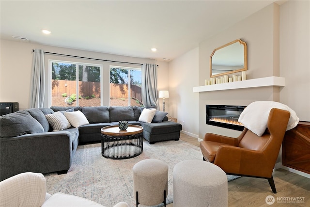 living area featuring a glass covered fireplace, recessed lighting, baseboards, wood finished floors, and visible vents
