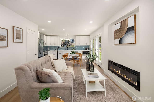 living area featuring a glass covered fireplace, baseboards, recessed lighting, and wood finished floors