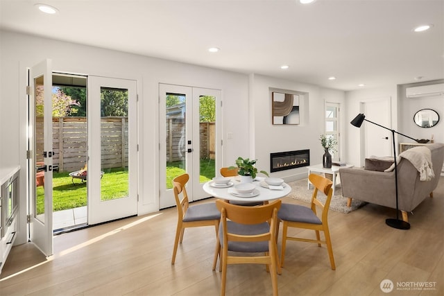 dining area with a wall unit AC, french doors, a wealth of natural light, and light wood-style floors