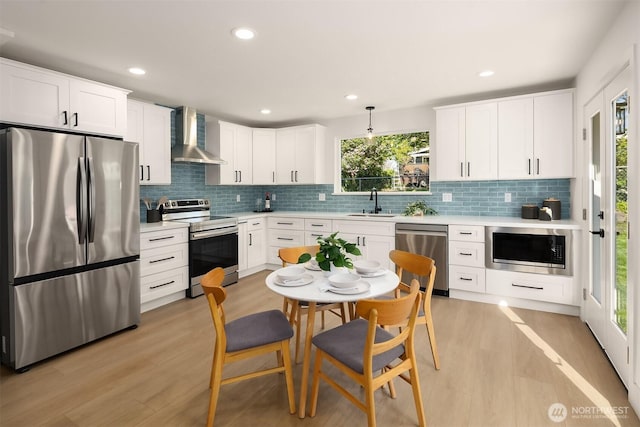 kitchen featuring wall chimney range hood, appliances with stainless steel finishes, backsplash, and light wood-type flooring