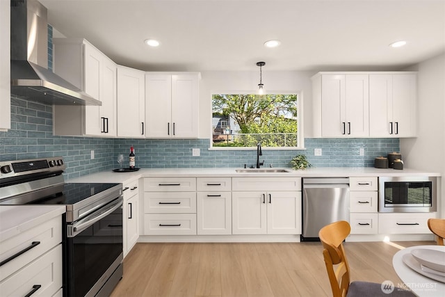 kitchen featuring a sink, wall chimney exhaust hood, appliances with stainless steel finishes, and light countertops