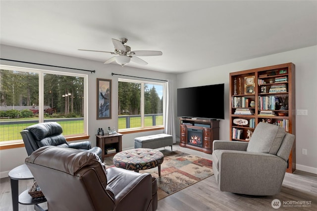 living room featuring a glass covered fireplace, ceiling fan, and wood finished floors