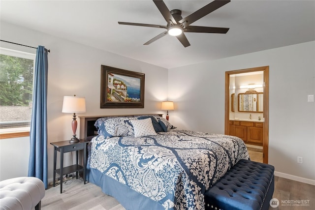 bedroom with a ceiling fan, wood finished floors, baseboards, ensuite bathroom, and a sink