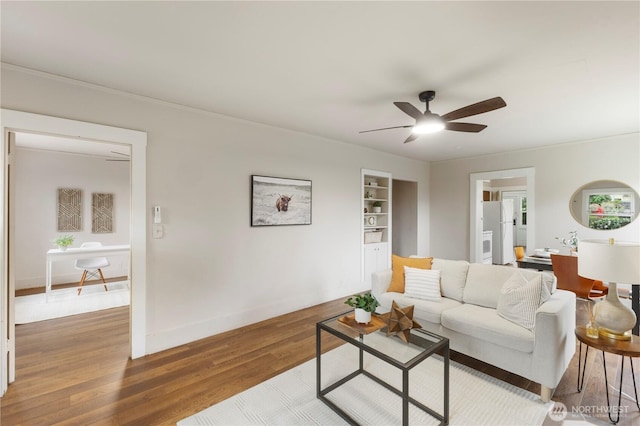 living area with baseboards, ceiling fan, wood finished floors, and built in shelves