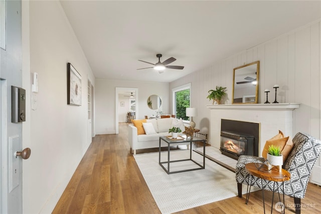 living area featuring baseboards, a ceiling fan, a glass covered fireplace, and wood finished floors