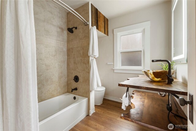 full bathroom with shower / bath combo, wood finished floors, a sink, baseboards, and toilet