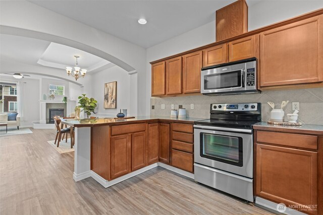 kitchen featuring appliances with stainless steel finishes, brown cabinets, a peninsula, open floor plan, and light wood-style flooring