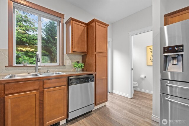 kitchen with light wood-style floors, baseboards, tasteful backsplash, a sink, and appliances with stainless steel finishes