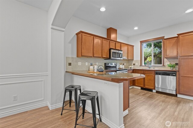 kitchen with a breakfast bar area, stainless steel appliances, and brown cabinetry