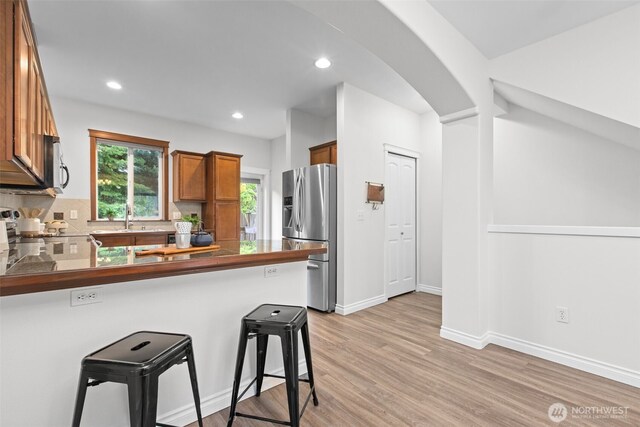 kitchen featuring appliances with stainless steel finishes, dark countertops, brown cabinets, a sink, and a peninsula