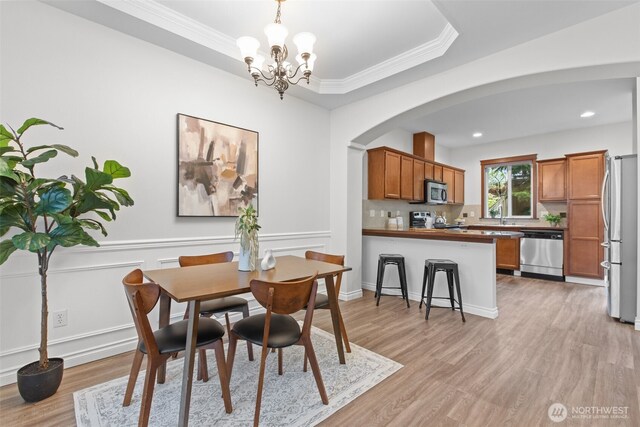 dining room with crown molding, arched walkways, light wood finished floors, and a chandelier