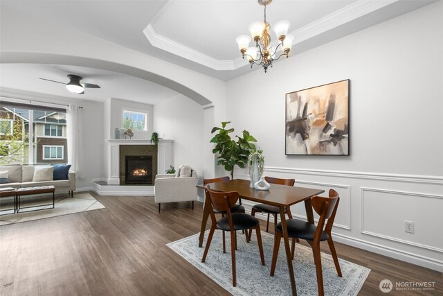 dining space featuring arched walkways, dark wood-style flooring, a lit fireplace, and ornamental molding