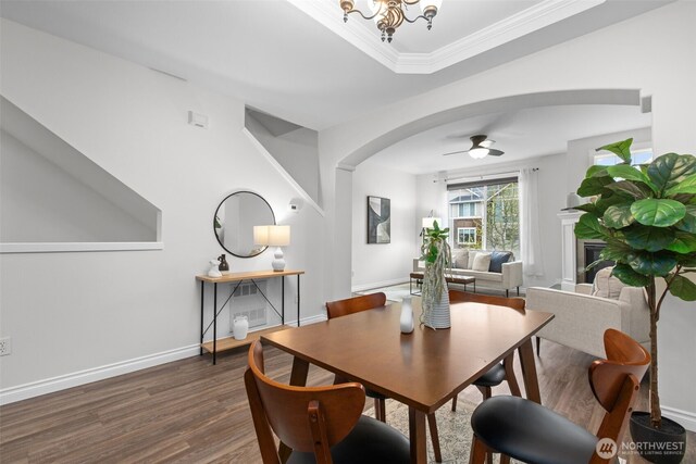 dining area with dark wood-style flooring, crown molding, arched walkways, baseboards, and ceiling fan with notable chandelier