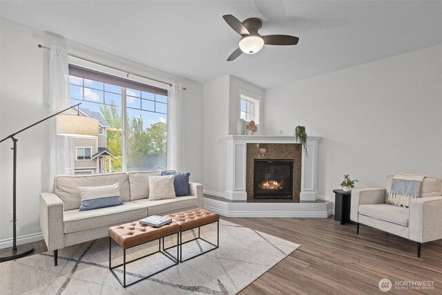 living room featuring a ceiling fan, baseboards, a glass covered fireplace, and wood finished floors