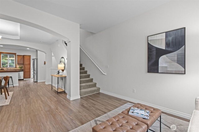 living area featuring baseboards, arched walkways, light wood-style flooring, and stairs