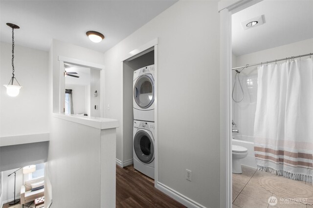 laundry room with ceiling fan, laundry area, wood finished floors, stacked washing maching and dryer, and baseboards