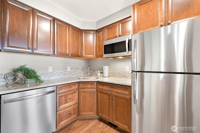 kitchen with brown cabinets, light stone counters, a sink, light wood finished floors, and stainless steel appliances