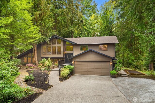 split foyer home featuring an attached garage, roof with shingles, a forest view, and concrete driveway
