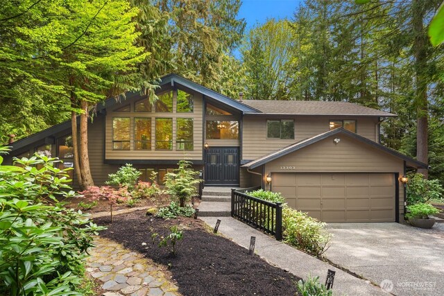 bi-level home with roof with shingles, an attached garage, and concrete driveway