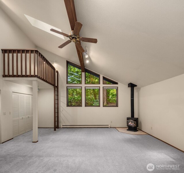 additional living space with baseboard heating, a wood stove, vaulted ceiling with skylight, carpet, and a ceiling fan