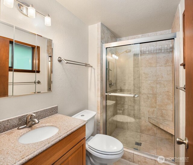 full bath with a textured wall, vanity, toilet, a textured ceiling, and a stall shower