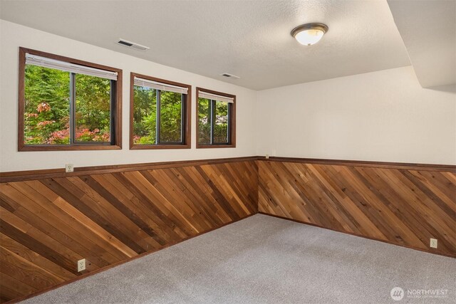 unfurnished room featuring wooden walls, carpet, and visible vents