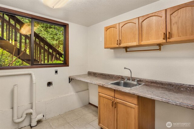 clothes washing area featuring electric dryer hookup, a sink, cabinet space, and a textured ceiling
