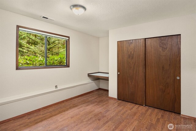 unfurnished bedroom featuring visible vents, a closet, wood finished floors, baseboards, and built in desk