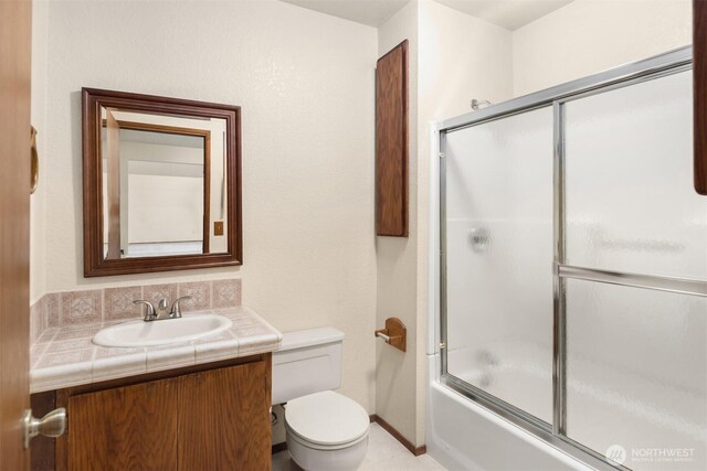 bathroom with toilet, baseboards, combined bath / shower with glass door, and vanity