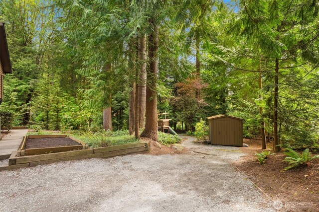 view of yard with a storage unit, an outdoor structure, a view of trees, and a garden