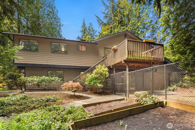 rear view of property featuring fence, stairs, a garden, and a wooden deck