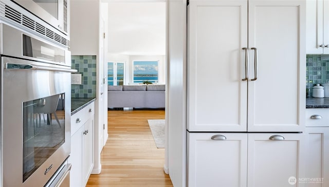 8012 Chinook Way, Blaine, WA 98230 - kitchen with dark countertops, light wood-type flooring, white cabinetry, stainless steel microwave, and tasteful backsplash