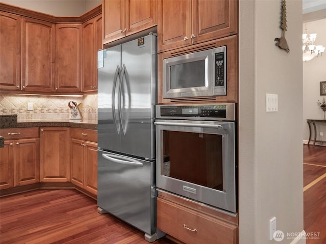 kitchen with brown cabinets, wood finished floors, tasteful backsplash, and stainless steel appliances