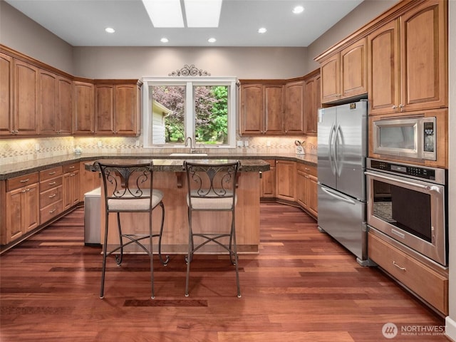 kitchen with a kitchen island, dark wood-style floors, a kitchen bar, appliances with stainless steel finishes, and a skylight