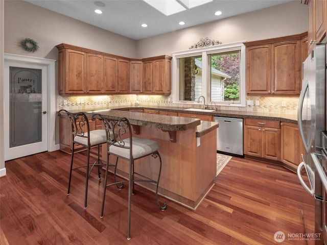 kitchen featuring dark wood-style flooring, a skylight, brown cabinets, a sink, and stainless steel appliances