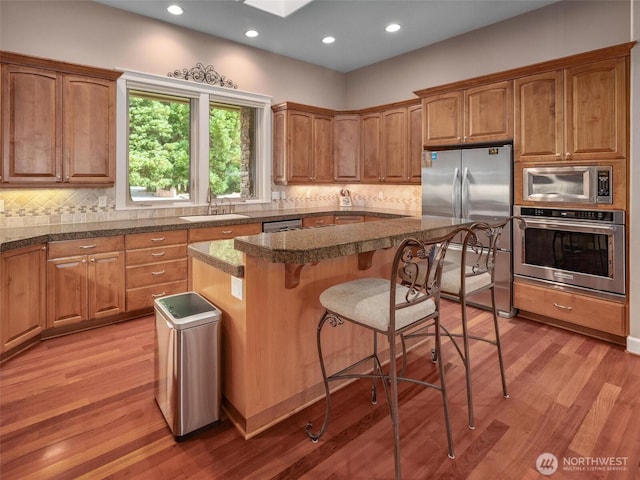 kitchen with appliances with stainless steel finishes, light wood-type flooring, a sink, a breakfast bar, and recessed lighting