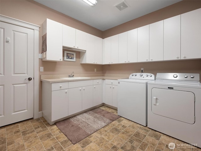 laundry room featuring a sink, cabinet space, stone finish flooring, and washing machine and clothes dryer