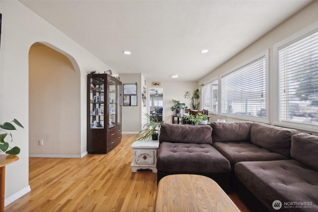 living room with arched walkways, baseboards, recessed lighting, and light wood-style floors