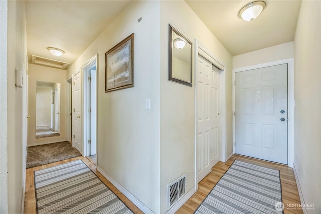 hallway with baseboards, attic access, light wood-type flooring, and visible vents