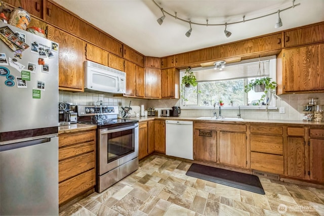 kitchen featuring appliances with stainless steel finishes, brown cabinetry, a sink, and tasteful backsplash
