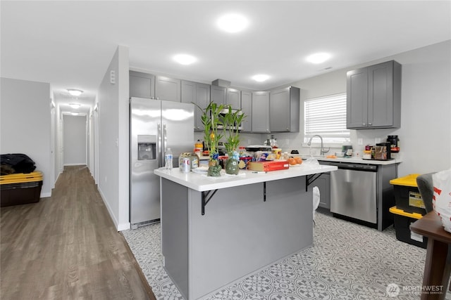 kitchen featuring a sink, light countertops, a breakfast bar area, stainless steel appliances, and gray cabinetry