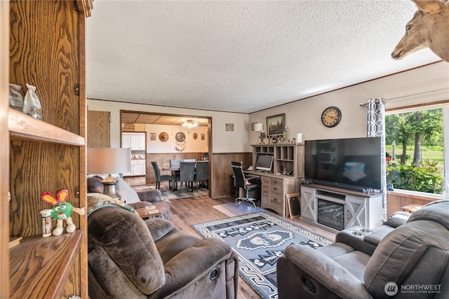living area featuring wainscoting, wood walls, a textured ceiling, and wood finished floors