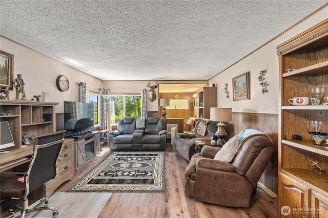 living room featuring wooden walls, a textured ceiling, wainscoting, and wood finished floors