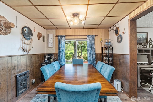dining space featuring heating unit, a wainscoted wall, wood walls, and wood finished floors