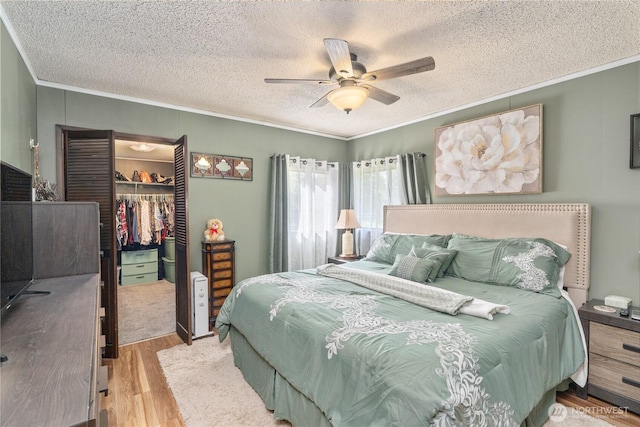 bedroom featuring a closet, ornamental molding, wood finished floors, ceiling fan, and a textured ceiling
